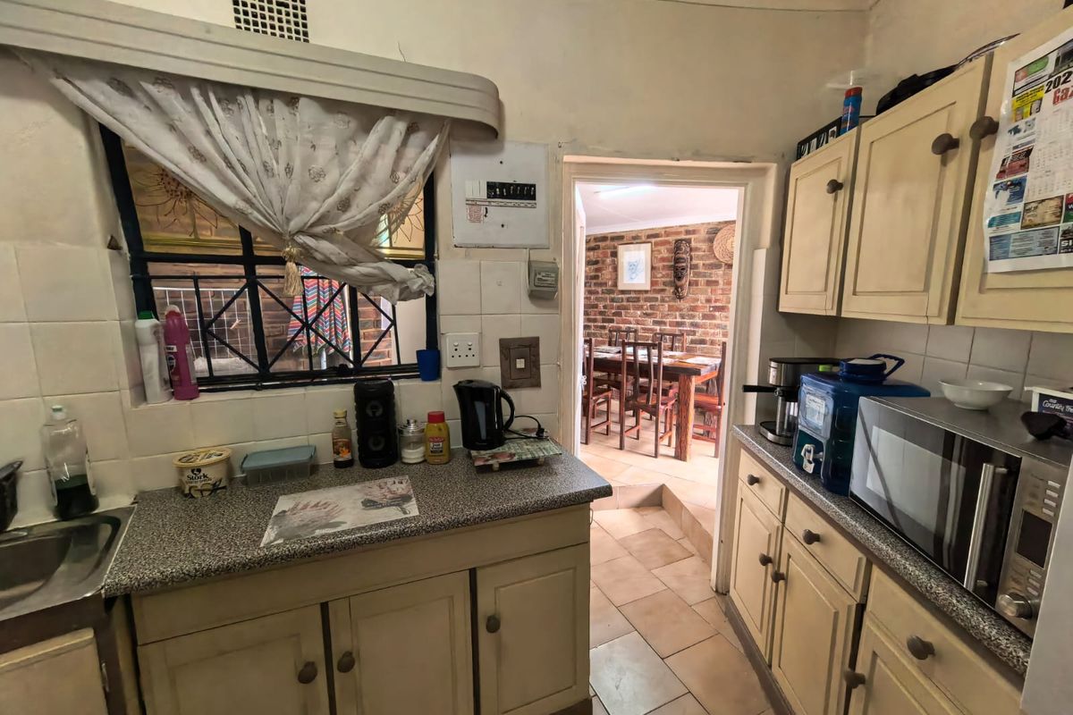 A compact kitchen featuring laminate cabinetry, tiled splashbacks, and a stainless steel sink, with a doorway leading to an adjacent dining area.