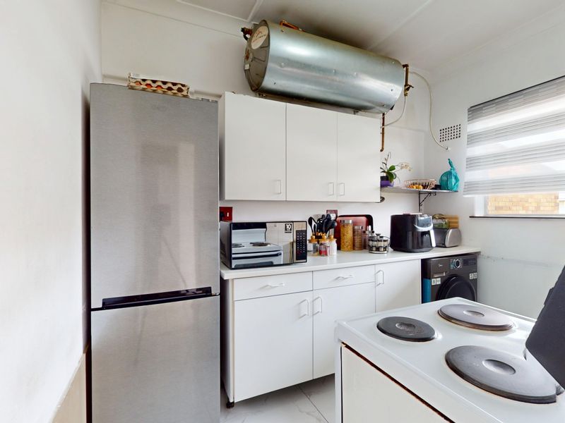Compact kitchen featuring white cabinetry, laminate countertops, and an electric stove, with an exposed hot water cylinder mounted above the upper cabinets.
