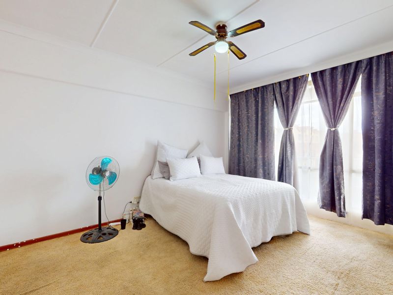 A bedroom featuring a ceiling fan, built-in wardrobe, and carpet flooring, offering a functional space with potential for cosmetic updates.