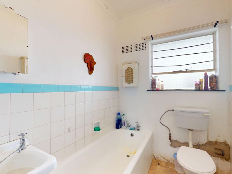 A dated bathroom featuring a bathtub, wall-mounted basin, and toilet, requiring renovation to address wall plaster damage and modernize the finishes.
