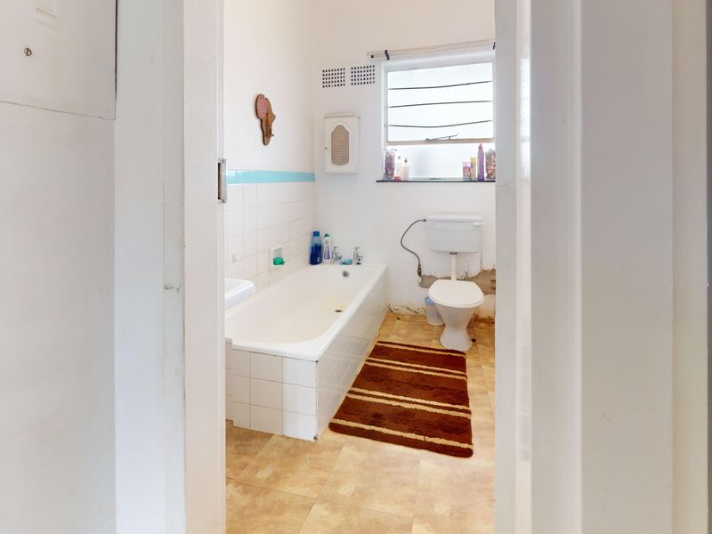 A dated bathroom featuring a standard bathtub, toilet, and louvered window, requiring renovation to address wall damage and worn finishes.
