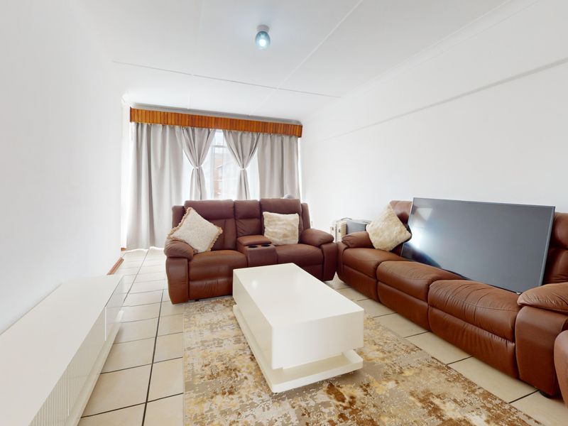 A bright living room featuring neutral tiled flooring and a window with a wooden pelmet finish.