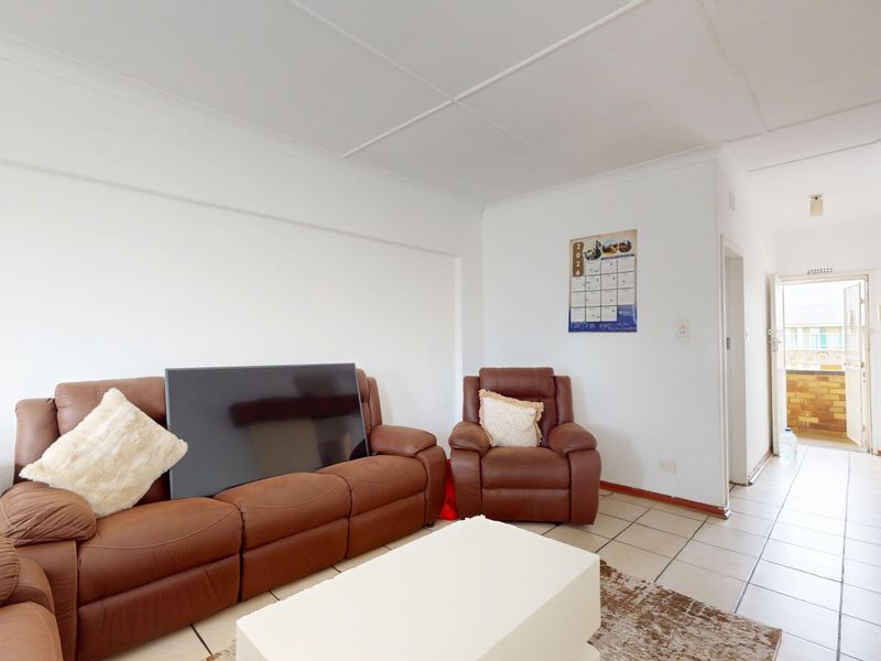 A living room area featuring tiled flooring and coved ceilings, leading to an entrance hallway.