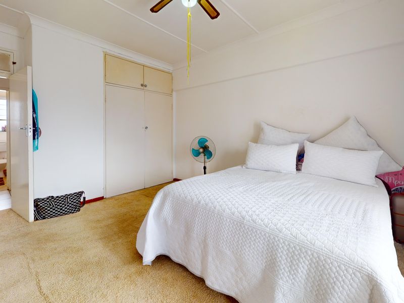 A bedroom featuring built-in cupboards, a ceiling fan, and carpeted flooring, with an adjoining bathroom visible through the doorway.