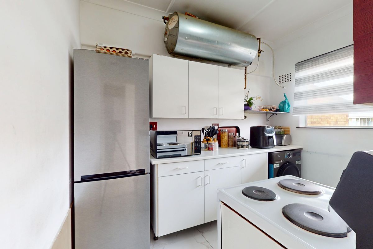 Compact kitchen featuring white cabinetry, laminate countertops, and an electric stove, with an exposed hot water cylinder mounted above the upper cabinets.