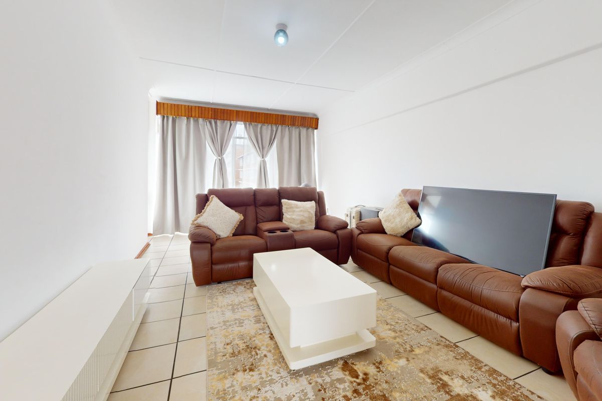 A bright living room featuring neutral tiled flooring and a window with a wooden pelmet finish.