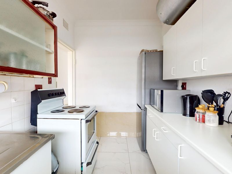A functional kitchen featuring white cabinetry, tiled backsplash, and a freestanding stove, offering a clean and practical layout for daily meal preparation.