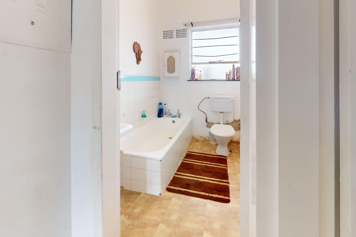 A dated bathroom featuring a standard bathtub, toilet, and louvered window, requiring renovation to address wall damage and worn finishes.