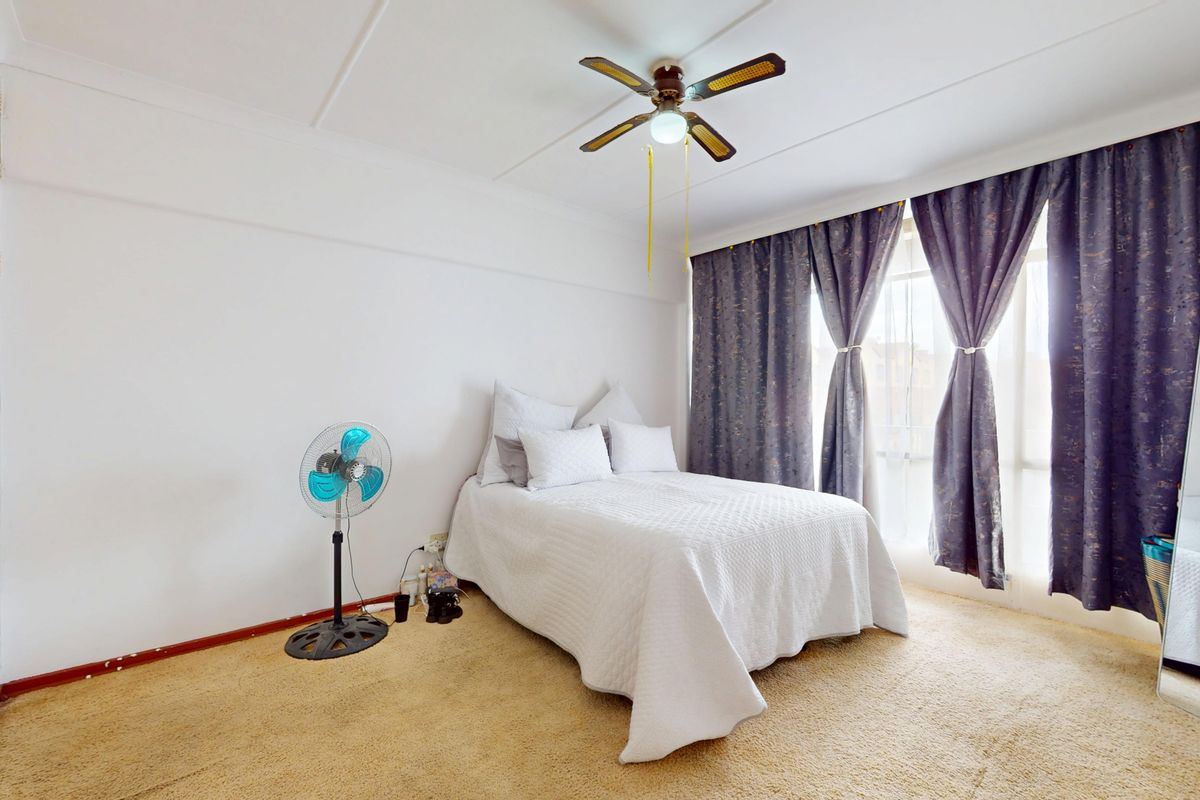 A bedroom featuring a ceiling fan, built-in wardrobe, and carpet flooring, offering a functional space with potential for cosmetic updates.