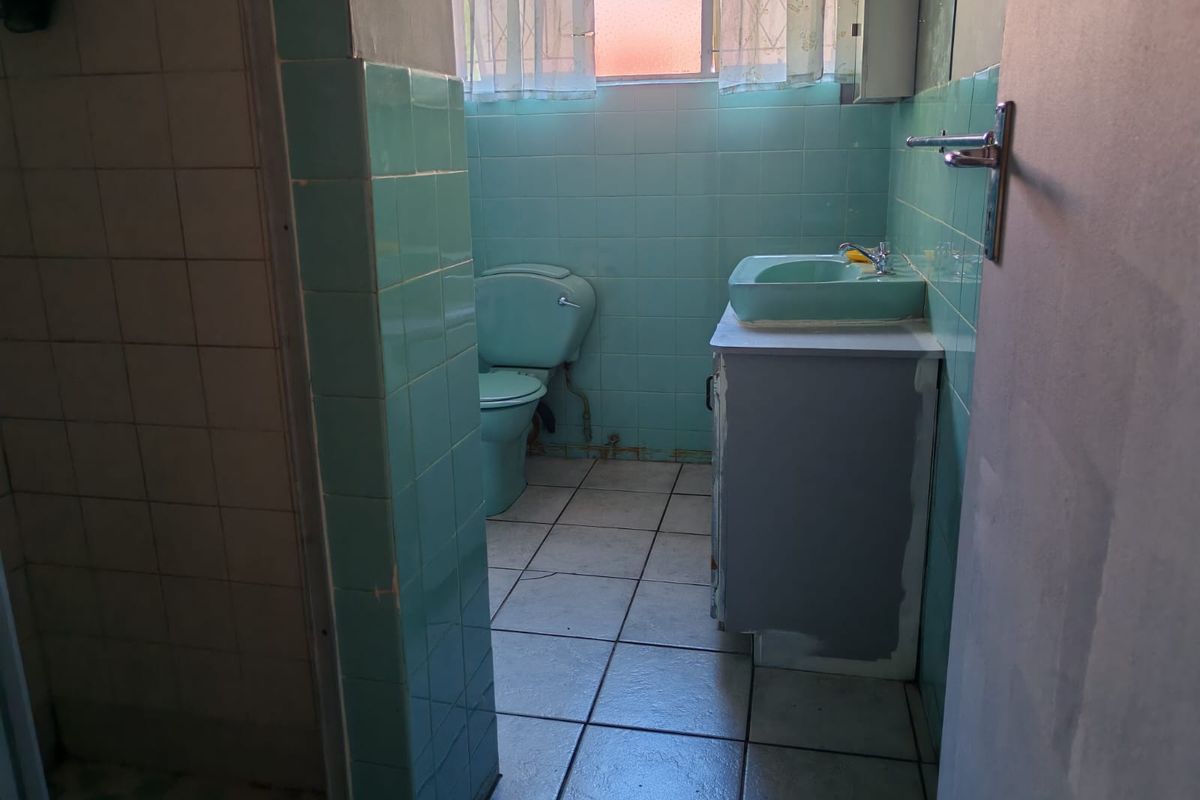 A dated bathroom featuring original pastel green tiling, a matching basin and toilet, and a separate shower enclosure.