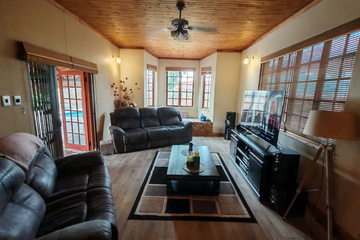 A comfortable living room featuring a warm timber-clad ceiling, laminate flooring, and a bay window, with direct access to the outdoor pool area.