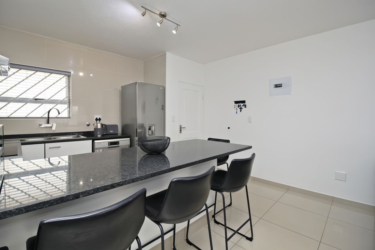 Modern kitchen featuring granite countertops, tiled splashback, and sleek cabinetry with a functional breakfast bar area.