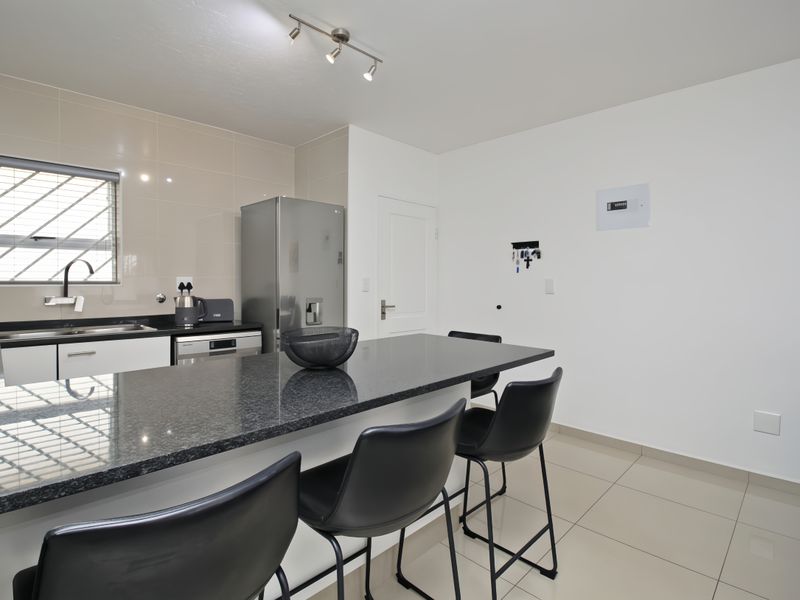 Modern kitchen featuring granite countertops, tiled splashback, and sleek cabinetry with a functional breakfast bar area.