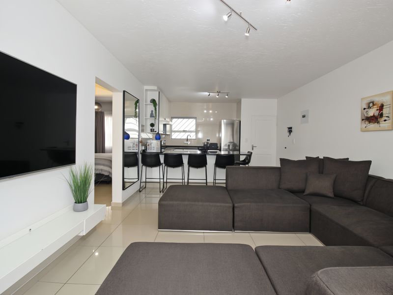 Modern open-plan living area featuring a sleek kitchen with island seating, tiled floors, and contemporary track lighting throughout the space.