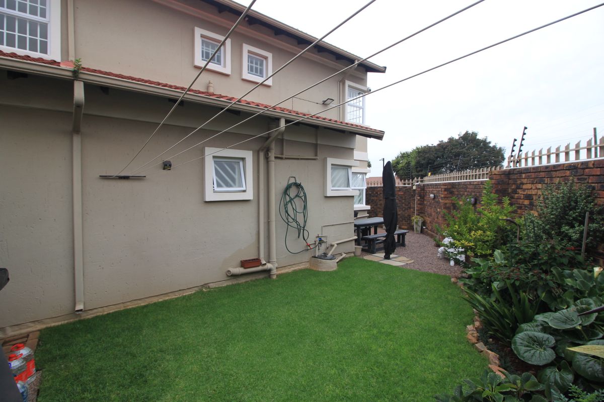 Rear exterior view of the property featuring a small lawn, brick boundary wall, and fixed washing line infrastructure.