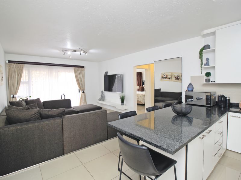 Modern open-plan living area featuring a sleek kitchen with granite countertops, tiled flooring, and seamless flow to the lounge space.