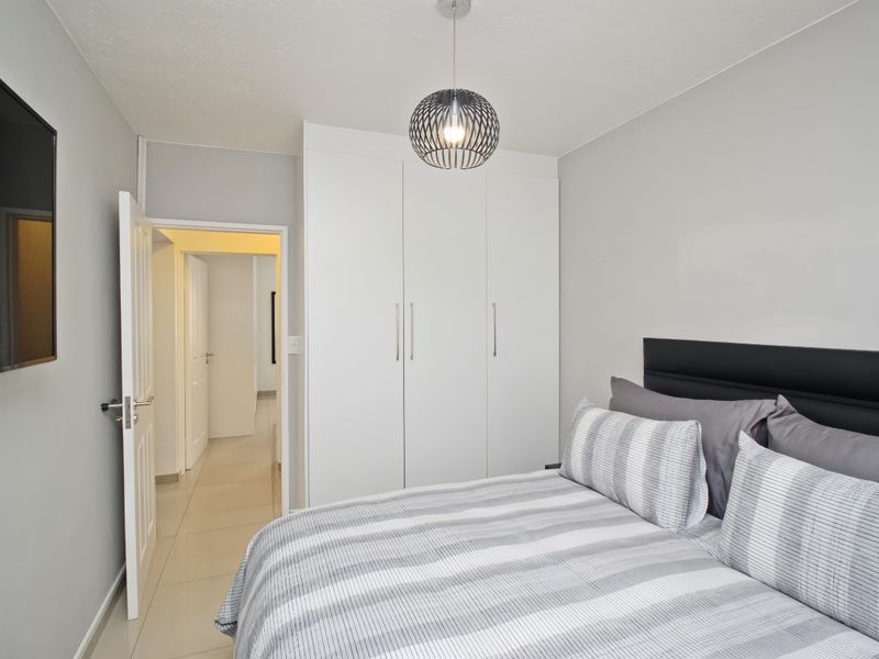 A well-maintained bedroom featuring neutral walls, tiled flooring, and ample built-in cupboard storage, providing a clean and functional living space.