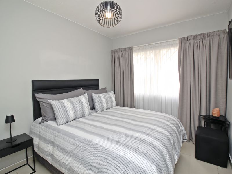 A well-maintained bedroom featuring neutral wall tones, tiled flooring, and large windows dressed with floor-to-ceiling curtains.