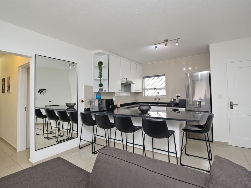 Modern open-plan kitchen featuring sleek white cabinetry, granite countertops, and a breakfast bar, seamlessly integrated into the living space.