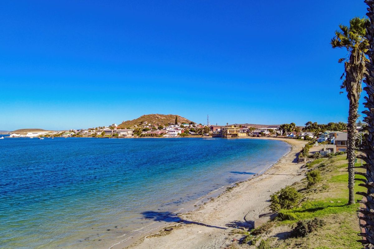 A scenic aerial view of the coastal landscape, featuring a sandy beach, clear blue water, and the surrounding town.