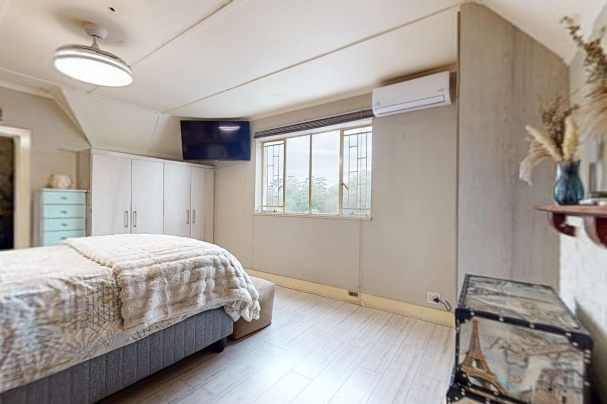 A bedroom featuring built-in cupboards, a split-system air conditioner, and laminate flooring, with security bars on the window.