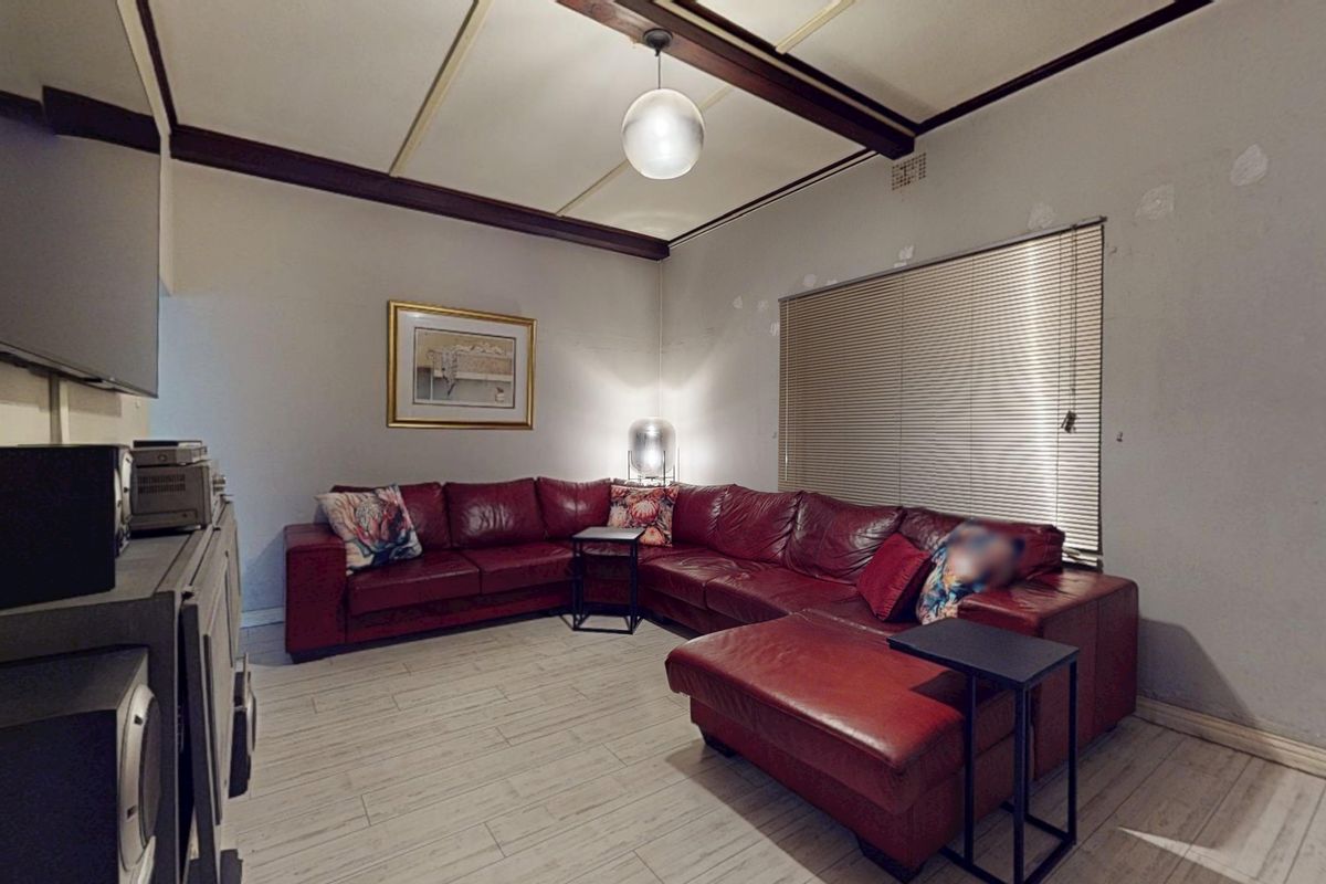 Living room featuring exposed timber ceiling beams, tiled flooring, and venetian blinds. The walls show signs of wear and require cosmetic attention.