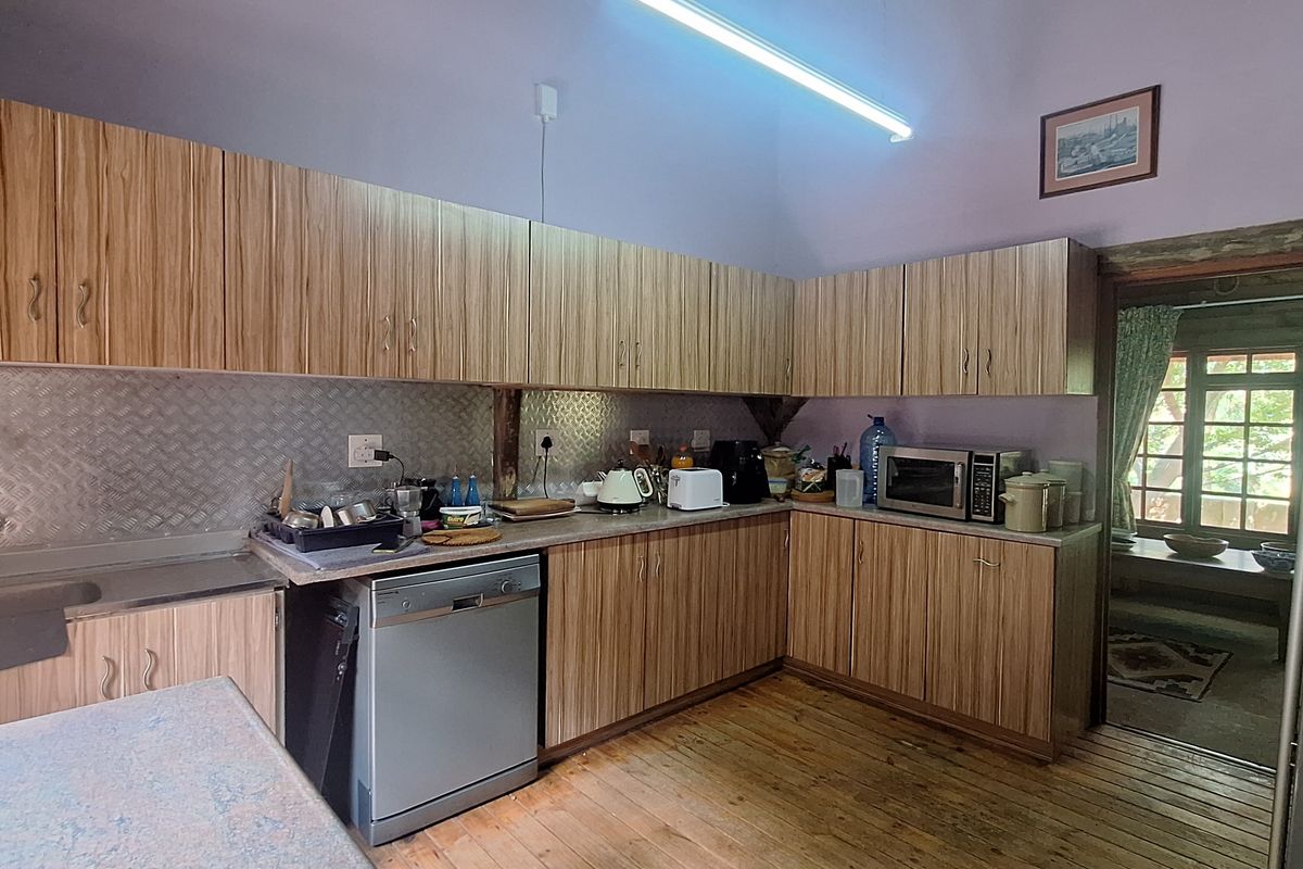 A rustic kitchen featuring timber cabinetry, metal splashbacks, and exposed rafters, with direct access to an adjoining room.