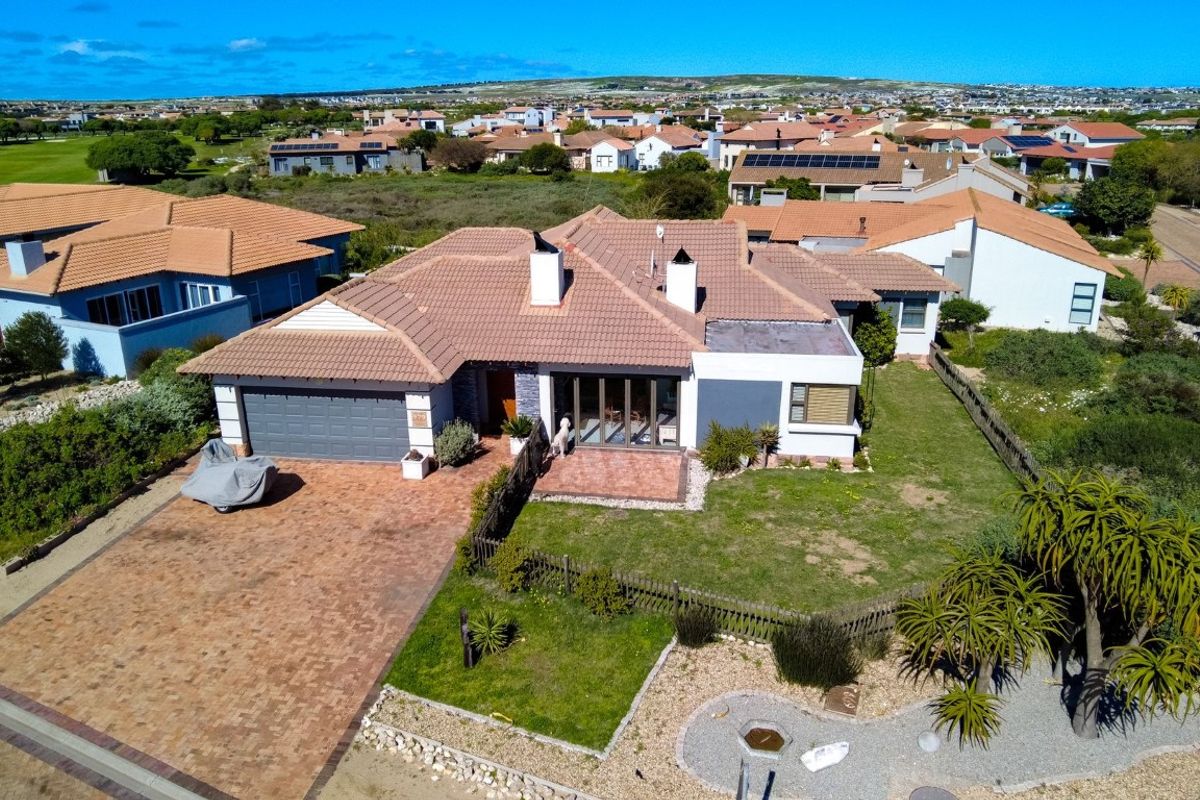 Aerial view of a residential property featuring a tiled roof, brick driveway, double garage, and a private garden with a paved patio area.