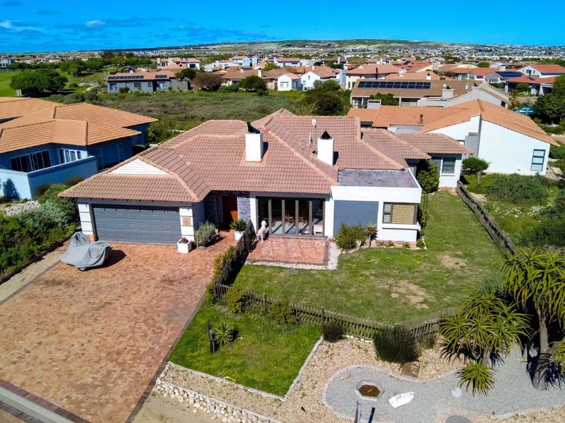 Aerial view of a residential property featuring a tiled roof, brick driveway, double garage, and a private garden with a paved patio area.