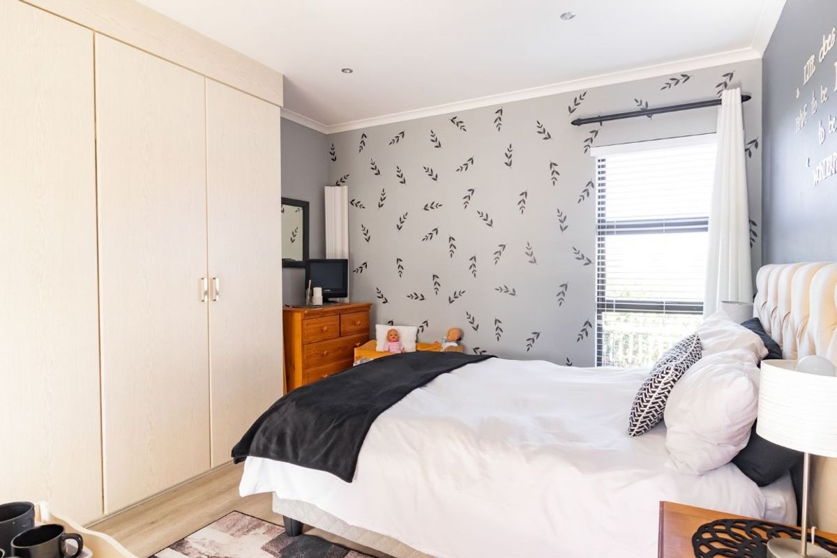 A well-maintained bedroom featuring neutral wood-grain built-in wardrobes, recessed downlighting, and a large window with fitted blinds.