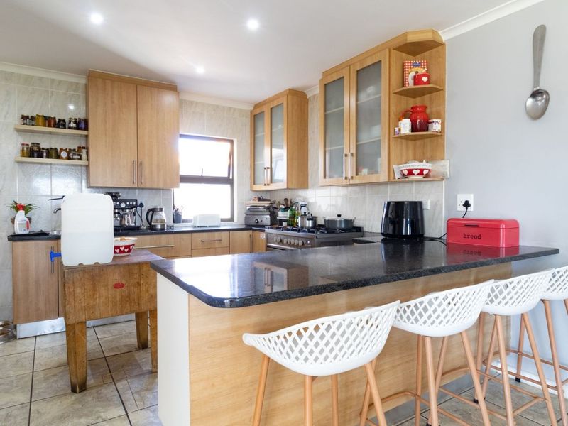 A functional kitchen featuring light wood cabinetry, granite countertops, a breakfast bar, and a tiled backsplash with integrated gas stove and recessed lighting.