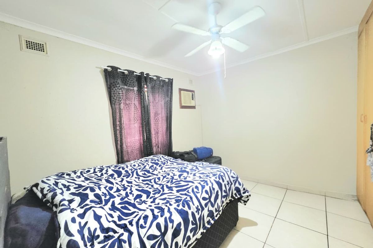 A functional bedroom featuring tiled flooring, a ceiling fan, built-in wardrobe storage, and a wall-mounted air conditioning unit.