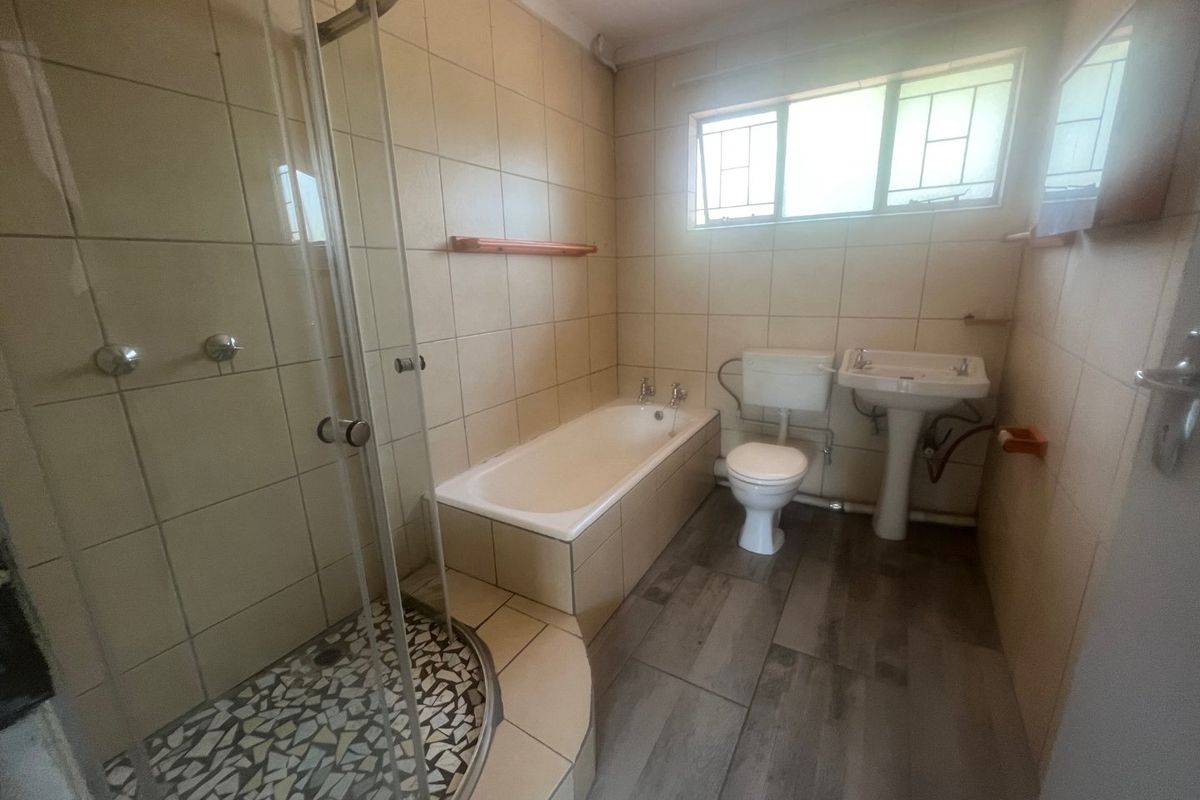 A functional bathroom featuring a separate shower enclosure, a built-in bathtub, a pedestal sink, and a toilet with neutral wall tiling and wood-look floor tiles.