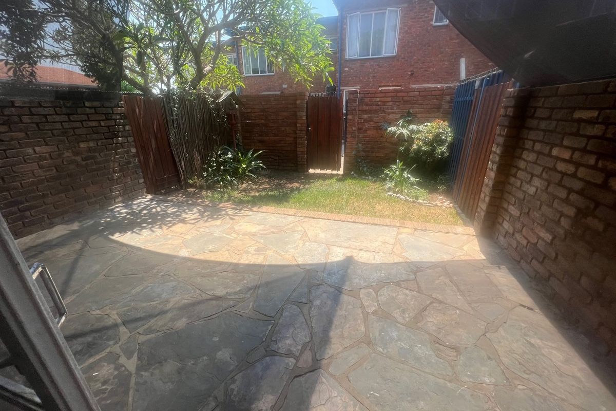 A private rear courtyard featuring natural stone paving, brick boundary walls, and a small garden area with a wooden gate.