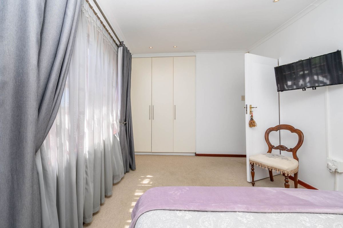 A well-maintained bedroom featuring neutral carpeting, built-in cupboards, and recessed downlighting, offering a clean and functional living space.