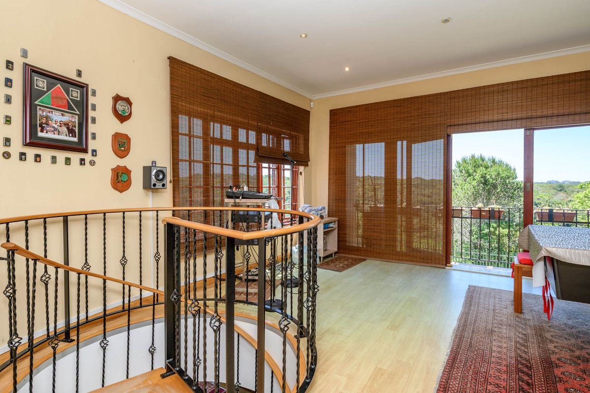 Spacious living area featuring a wrought iron staircase, laminate flooring, and sliding glass doors leading to a balcony with scenic views.