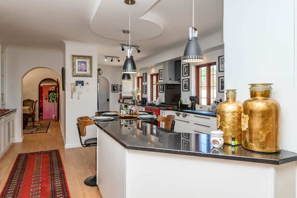 Spacious kitchen featuring a large granite island, modern pendant lighting, built-in appliances, and a distinctive architectural archway leading to adjacent living areas.