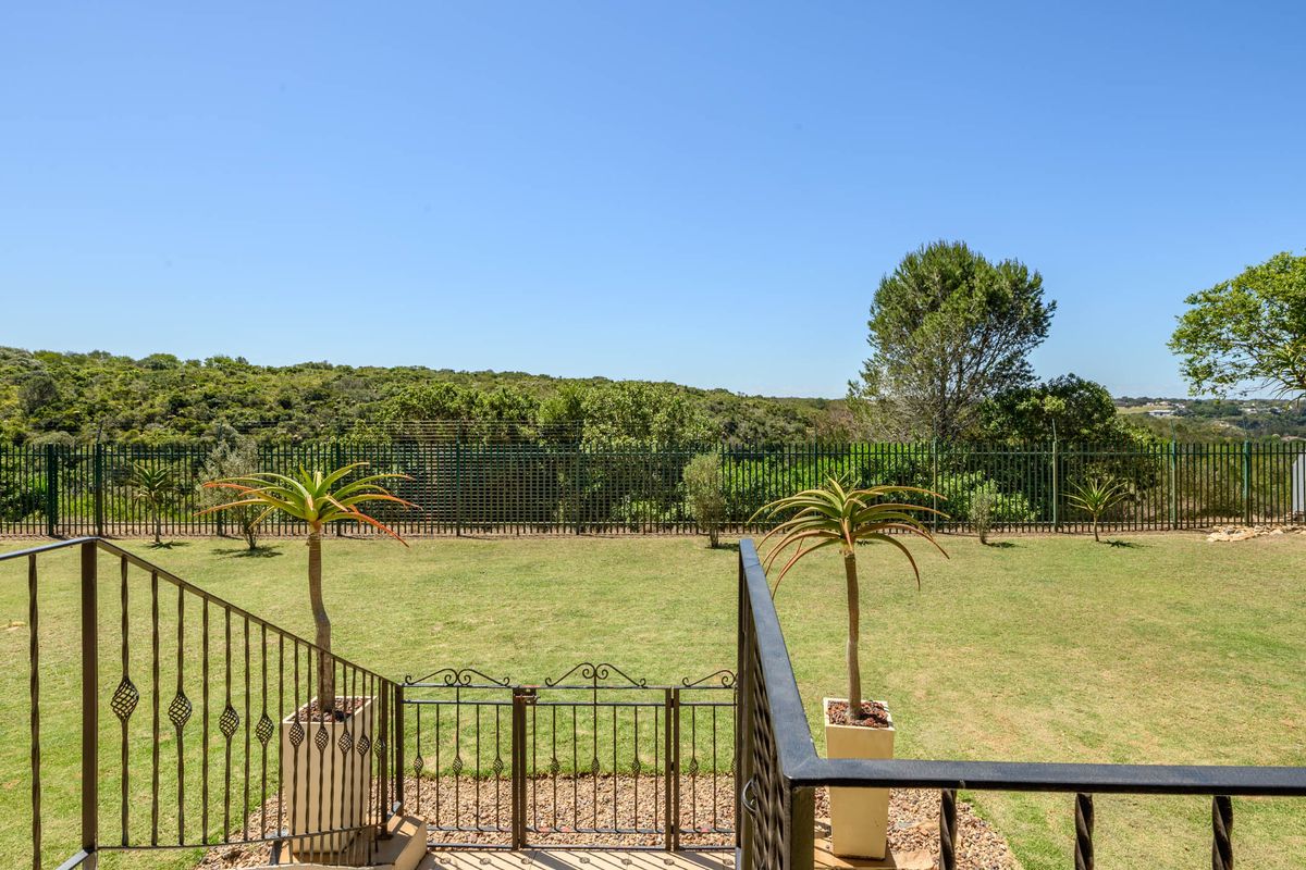 A well-maintained rear garden featuring a manicured lawn, metal perimeter fencing, and a wrought iron gate with a view of the surrounding landscape.
