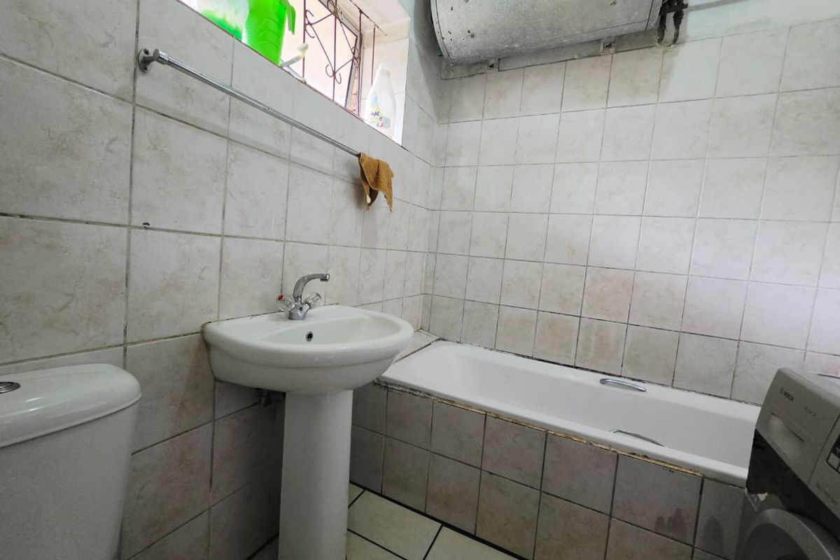 A functional bathroom featuring a pedestal sink, bathtub, and wall-mounted water heater, with tiled walls and flooring throughout.