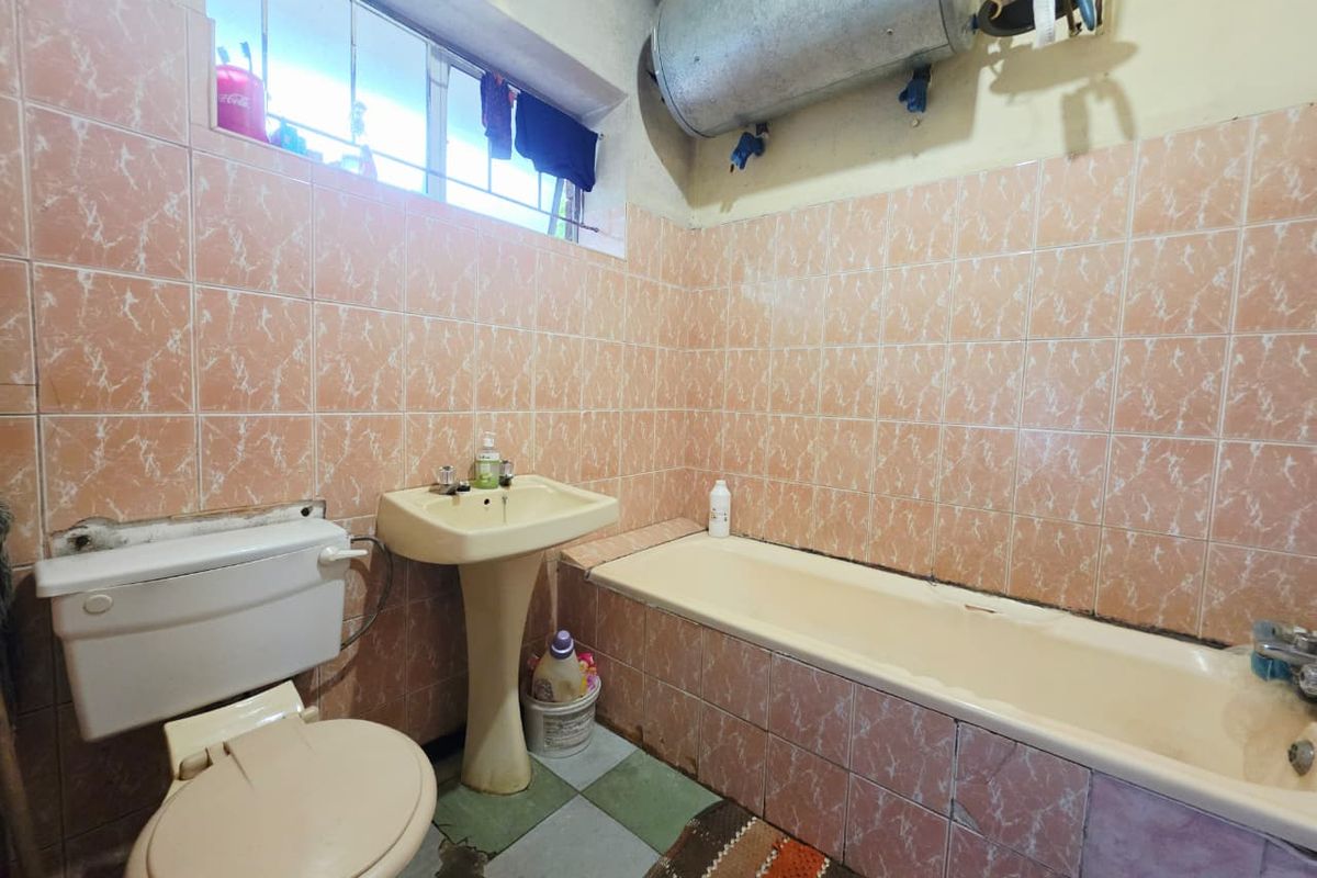 A dated bathroom featuring a pedestal basin, bathtub, and toilet, with wall-to-wall tiling and an exposed electric water heater.