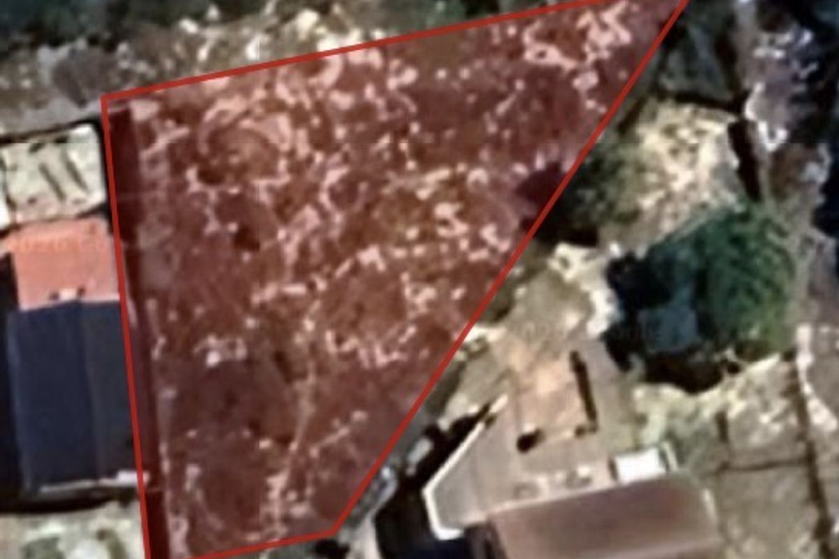 An aerial view of a vacant residential plot with a red boundary overlay indicating the property lines.