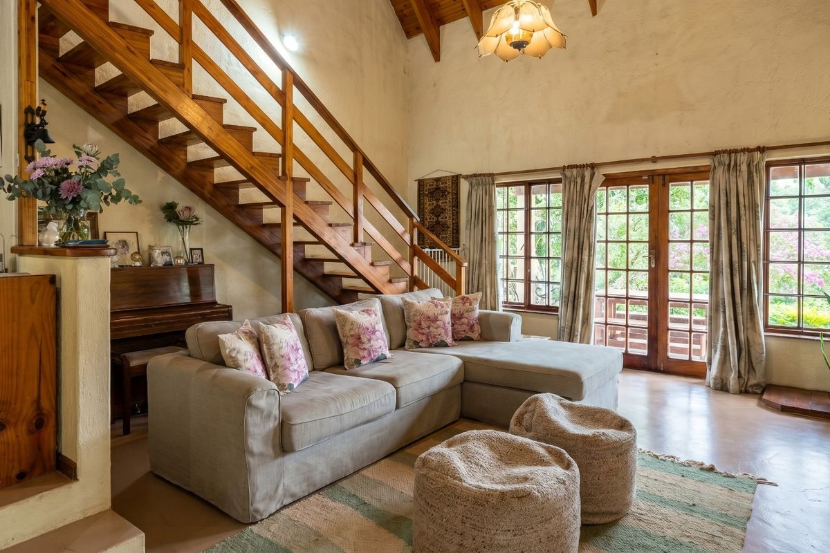 Spacious living room featuring high vaulted ceilings with exposed timber beams, a wooden staircase, and direct access to the outdoor patio through french doors.