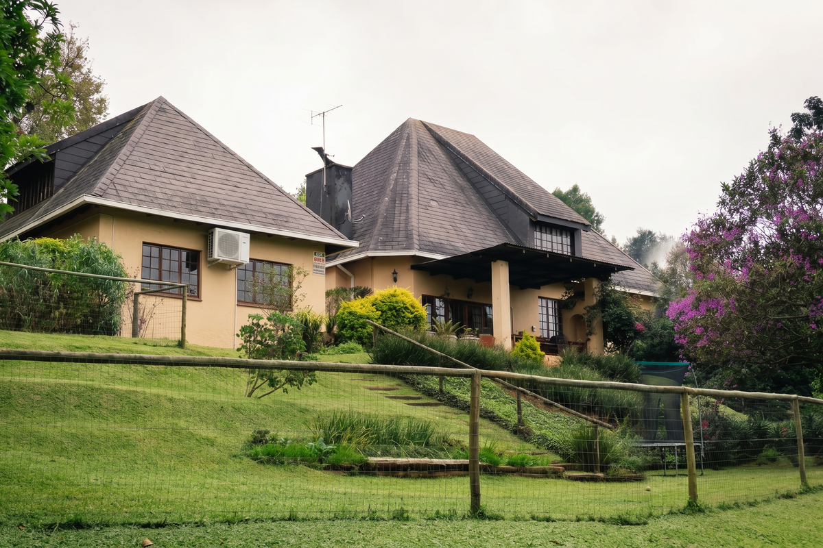 Rear view of a multi-level house featuring a pitched roof, covered patio area, and a sloped garden with timber fencing.