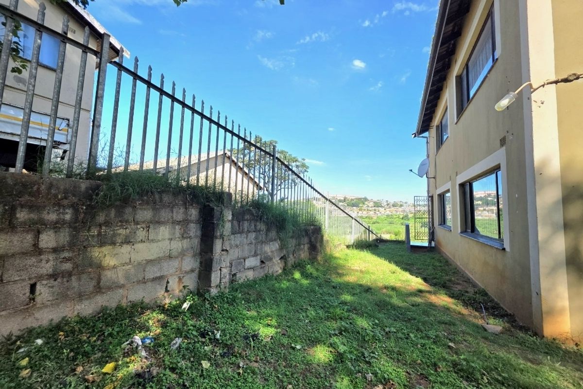 Rear exterior view of the property featuring a concrete block retaining wall, metal security fencing, and a side garden area.