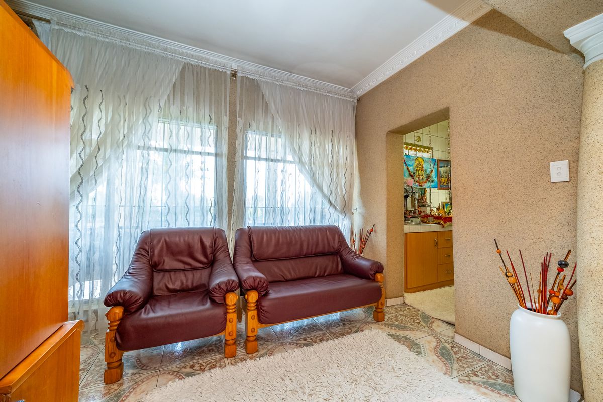 A living area featuring textured walls, decorative crown molding, and tiled flooring, with an adjacent view into a secondary kitchen or utility space.