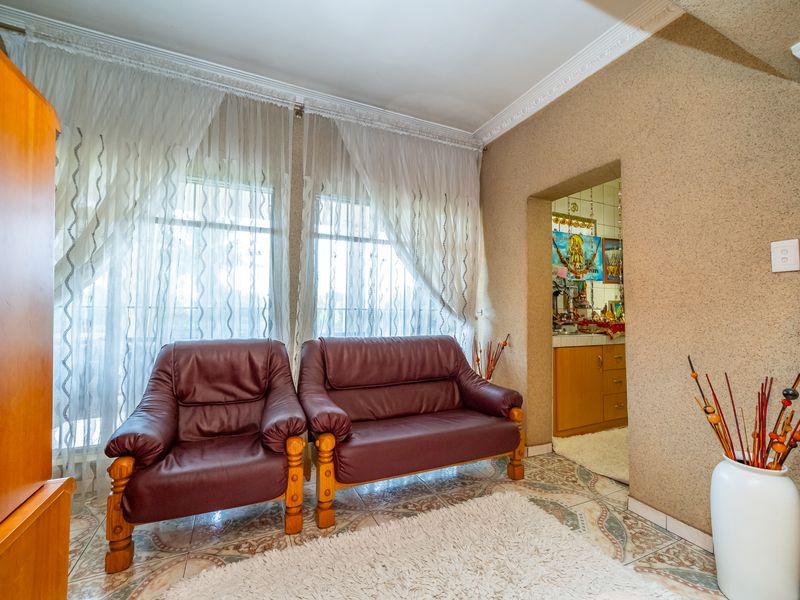 A living area featuring textured walls, decorative crown molding, and tiled flooring, with an adjacent view into a secondary kitchen or utility space.