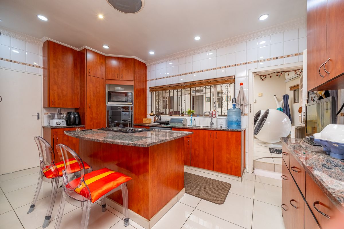 A functional kitchen featuring wood-veneer cabinetry, granite countertops, a central island with a built-in hob, and tiled flooring throughout.