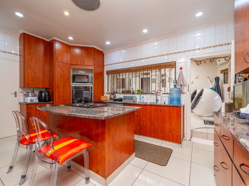 A functional kitchen featuring wood-veneer cabinetry, granite countertops, a central island with a built-in hob, and tiled flooring throughout.