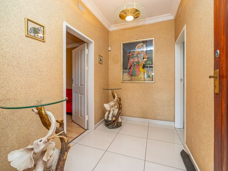 A bright entrance hallway featuring tiled flooring, textured wall finishes, and decorative ceiling cornicing, providing access to adjacent rooms.