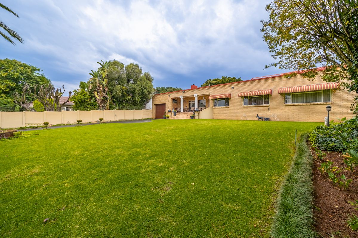 Spacious rear garden featuring a well-maintained lawn, perimeter wall, and a brick-faced house with a covered patio area.
